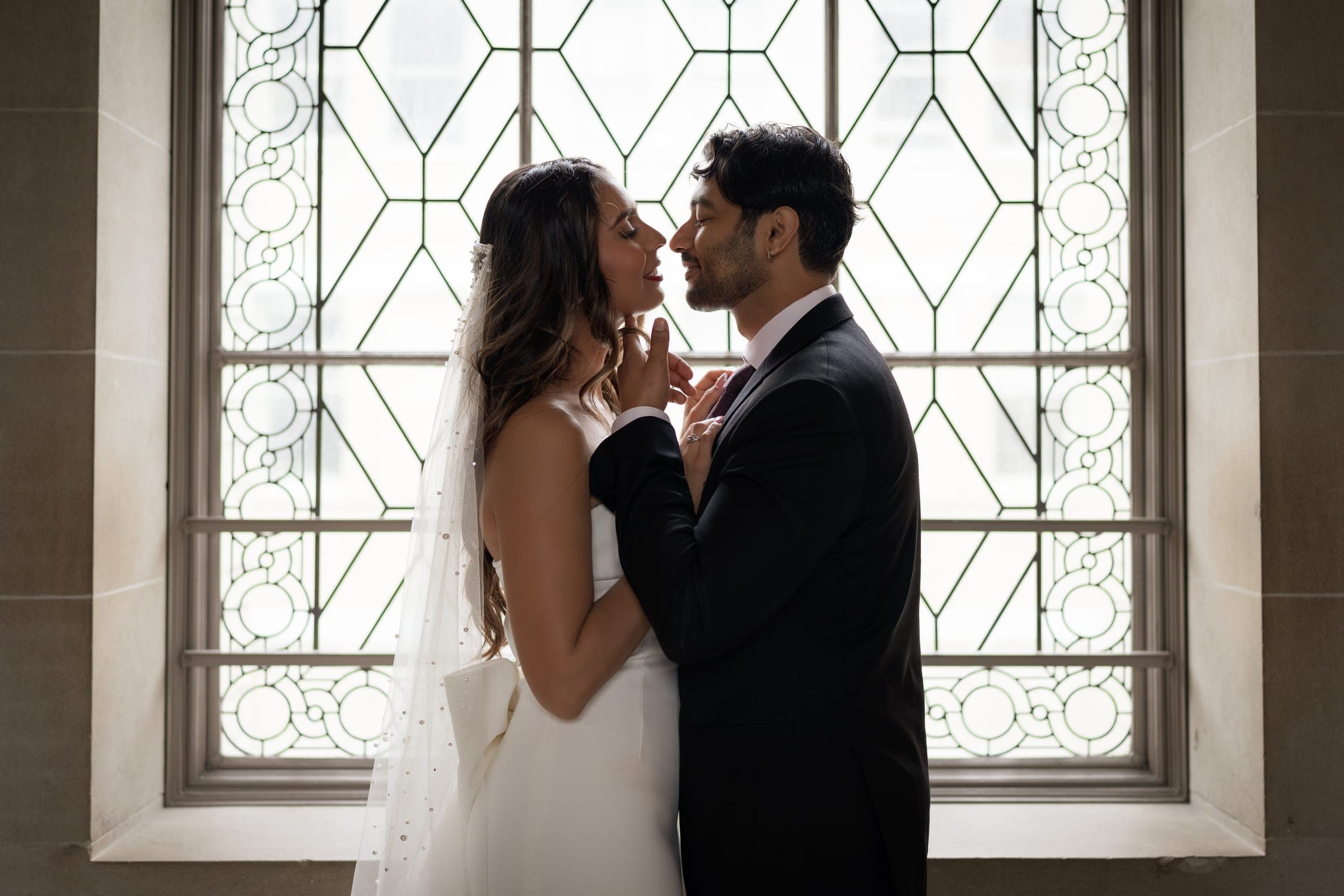 Bishal and Anna about to kiss in front of a leaded-glass window